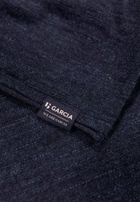 Dunkelblaues, strukturiertes Gewebe mit einem subtilen Muster; umfasst ein schwarzes Etikett mit der Aufschrift "GARCIA WE ARE GARCIA", das an der Kante befestigt ist.