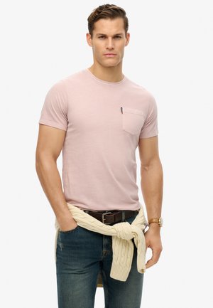 Lyserød bomulds t-shirt med korte ærmer og en brystlomme. Båret med mørkeblå denim jeans og en cremefarvet sweater bundet om livet.