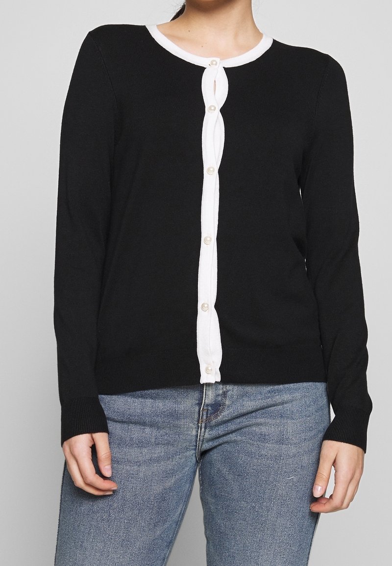 Svart långärmad kofta med vit knapplist och kant. Tillverkad av mjukt stickat material, med rund halsringning och ribbade ärmmuddar.