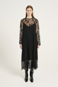 Svart spetsklänning med långa ärmar, en genomskinlig bodice, intrikata blommönster och en lång fåll. Kombinationen med knähöga blanka svarta stövlar.