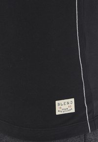 T-shirt nera in cotone con dettagli di cucitura bianchi, orlo inferiore arrotondato e un piccolo etichetta con il testo "BLEND 1993" di lato.