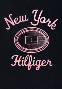 Černé tričko z látky s růžovým vyšívaným textem: "New York" nad oválným logem a "Hilfiger" pod ním, s liniovým detailem.