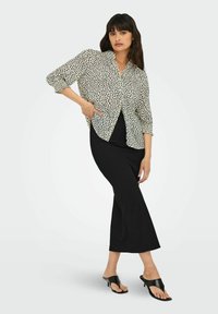 Lichte, gemusterde blouse met een losse fit en verlaagde schouders, gecombineerd met een strakke zwarte ribstof rok en zwarte sandalen met hak.