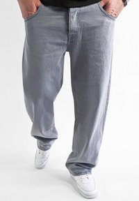 Gray denim pants feature a loose fit with side pockets. Worn with white sneakers, the fabric has a smooth texture and slight fading.