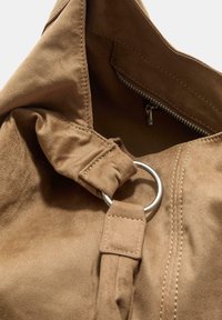 Interno della borsa in suede marrone con una tasca con cerniera, hardware in anello argento, texture morbida e dettagli cuciti. Modellata per la versatilità.