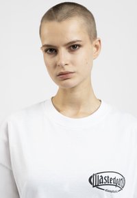 White cotton sweatshirt with a round neckline, featuring a black graphic logo on the left side. Smooth texture and casual fit.