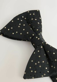 Black bow tie featuring a textured fabric with gold and silver polka dots, a classic butterfly shape, and a central knot detail.