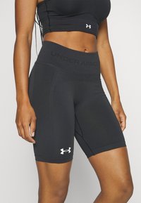 Czarne sportowe spodenki z wysokim stanem, wykonane z elastycznego materiału. Wyróżnia je logo "UNDER ARMOUR" i białe oznaczenie po lewej stronie.