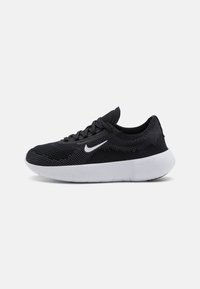 Zapatillas deportivas de malla negras con suela blanca. Presentan una punta redondeada, cordones y un sutil patrón texturizado en la parte superior. Logotipo de Nike visible.
