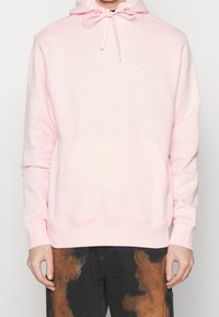 Ljusrosa hoodie med dragsko, framficka och vit Nike-logotyp. Tillverkad av mjukt material med ribbade muddar och fåll.