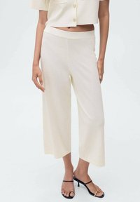 Pantalones de pierna ancha en color crema con una textura suave, que cuentan con una cinturilla elástica y un corte cropped, combinados con sandalias negras de tiras.