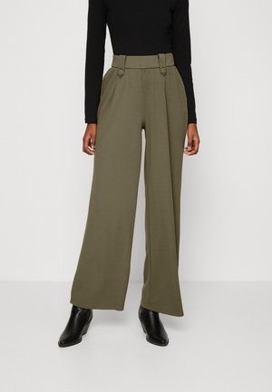 Wijd uitlopende olijfgroene broeken met een hoge taille en knoopaccenten, gemaakt van een gladde stof, gecombineerd met zwarte enkellaarsjes.