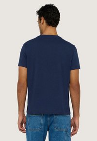 Camiseta de algodón de manga corta azul marino, con un diseño sencillo, cuello redondo y un bajo recto, combinada con unos vaqueros azul claro.