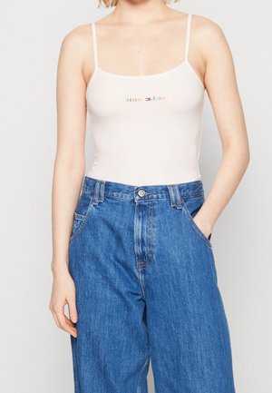 Canotta bianca con spalline sottili che presenta il logo "Tommy Jeans" in lettere colorate. Abbinata a jeans in denim blu a vestibilità rilassata.