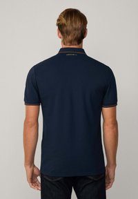 Polo azul marino con tejido liso, mangas cortas y cuello de doble raya. Presenta un logo dorado en la parte trasera del cuello.