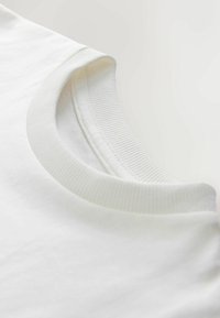 Vit bomull T-shirt med en ribbad rund halsringning och mjuk tygtextur. Minimalistisk design utan synliga mönster eller grafik.