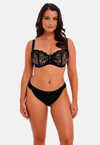 Sostén de encaje negro con paneles transparentes y bordados decorativos. Lencería negra a juego con bordes festoneados y pequeños adornos.