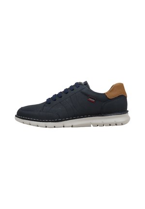 Zapatilla casual azul marino con suela blanca, lengüeta marrón en el talón y cordones azul marino, mostrada de lado.