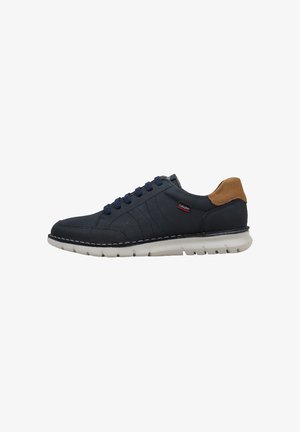 Zapatilla casual azul marino con suela blanca, lengüeta marrón en el talón y cordones azul marino, mostrada de lado.