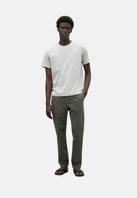 Camiseta de manga corta gris claro combinada con pantalones verdes oliva y sandalias negras. Diseño sencillo con un ajuste relajado.