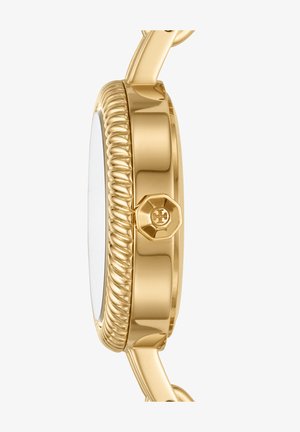 Côté d’un boîtier de montre en or avec une lunette texturée et une couronne octogonale ornée d’un emblème en forme de croix sur fond blanc.