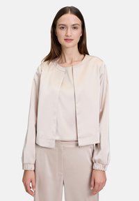 Helle beige satinierte cropped Jacke mit Rundhalsausschnitt, langen Ärmeln und elastischen Bündchen. Glatte Textur mit minimalistischem Design.