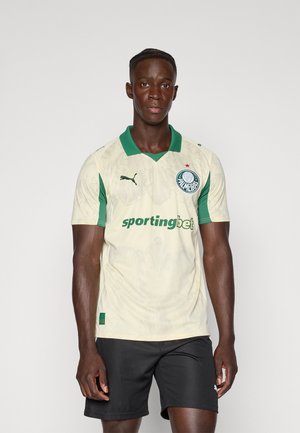 Lichtbeige sportshirt met groene accenten, met een v-hals, clublogo op de borst en de tekst "sportingbet". Korte mouwen.