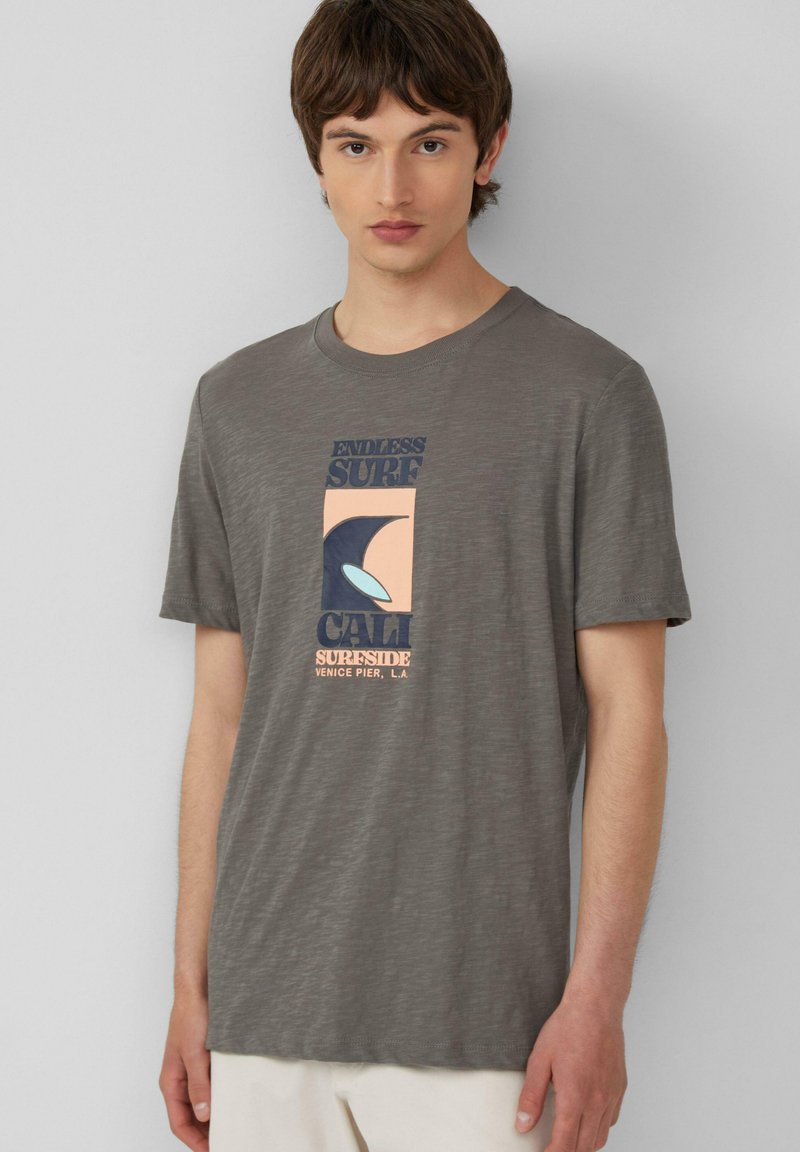 Graues T-Shirt mit kurzen Ärmeln aus weichem Stoff, das ein farbenfrohes Grafikdesign mit dem Text "Endless Surf" und Wellenmotiven zeigt.