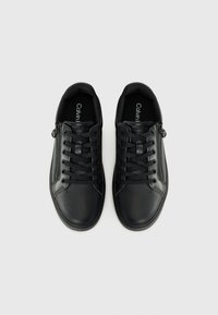 Par sorte læder lave sneakers med snørebånd og sidelommer, Calvin Klein branding indeni, vist ovenfra på hvid baggrund.