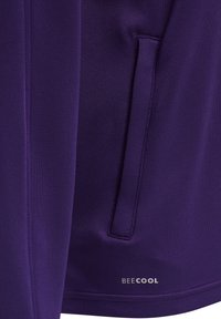 Fialová sportovní bunda s měkkou texturou, boční kapsou a logem "BEECOOL" na spodním lemu. Přiléhavý design, minimální švy.