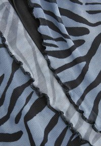 Tejido de malla en azul claro con un patrón de cebra negro, con un borde con volantes. La textura parece transpirable y ligera.