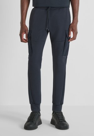 Pantalones jogger navy hechos de tela suave, con bolsillos tipo cargo, cinturilla con cordón y puños acanalados. Combinados con zapatillas negras.