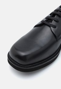 Zwarte leren schoen met een ronde neus, een gladde textuur en dunne veters. Beschikt over een gestikte zool voor duurzaamheid en strakke lijnen.