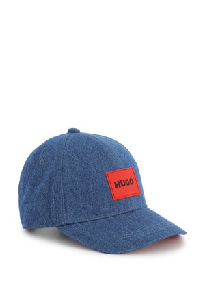 Casquette de baseball en denim bleu avec une patch rectangulaire rouge portant le mot "HUGO." Visière courbée et sangle ajustable à l'arrière.