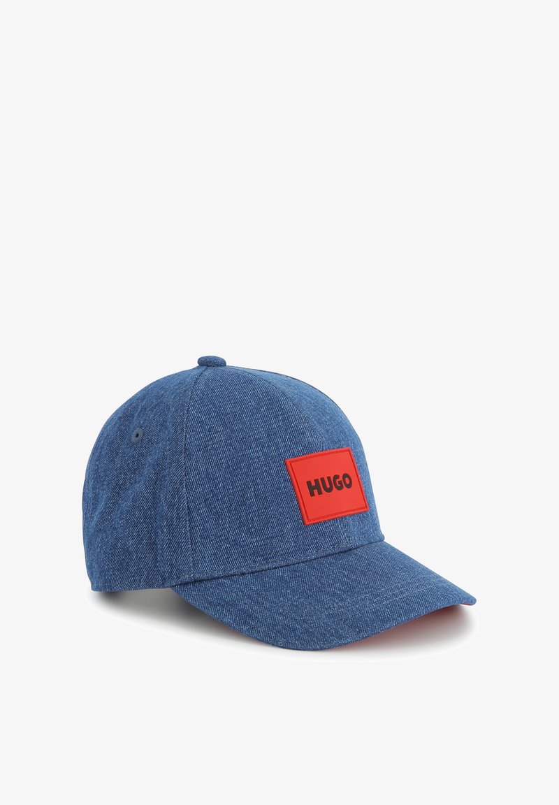 Casquette de baseball en denim bleu avec une patch rectangulaire rouge portant le mot "HUGO." Visière courbée et sangle ajustable à l'arrière.