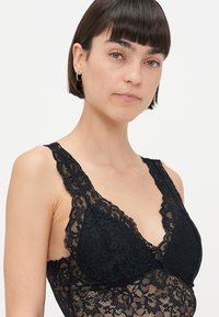 Mustikka pitsinen bralette, jossa on syvä V-avoinne, aaltoilevat pitsireunat ja säädettävät hihnat. Pehmeä tekstuuri kukkakuosisella pitsillä.