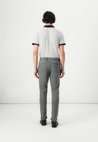 Striped polo shirt with navy collar, paired with gray slim-fit trousers. The outfit includes black shoes, showcasing a modern, casual look.