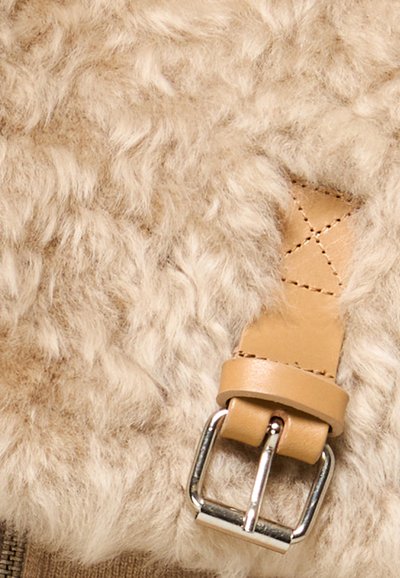 Fibbia in pelle marrone con puntale in metallo argentato attaccata a un tessuto di lana beige e soffice.