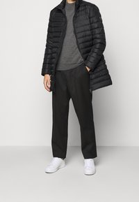 Svart puffjacka med horisontell quiltning, grå tröja med rund hals, svarta byxor och vita sneakers. Enkel, funktionell design.