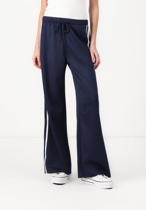 Pantalons larges bleu marine en tissu lisse, dotés de rayures blanches sur les côtés et d'une taille à cordon ajustable.