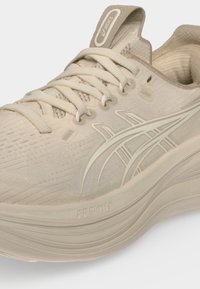 Μπεζ παπούτσι τρεξίματος ASICS με υφασμάτινο άνω μέρος με υφή, δέσιμο με κορδόνια και ορατή ενδιάμεση σόλα FF Blast+ για απορρόφηση κραδασμών.