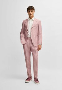 Completo di lino rosa chiaro con giacca a un petto e pantaloni dritti. Indossato su una camicia bianca, abbinato a scarpe da ginnastica bordeaux.