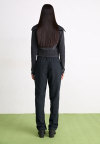 Svart mocka kort jacka och höga svarta byxor, matchade med klumpiga svarta platåskor. Slät textur och minimalistisk design.