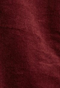 Tissu en velours côtelé bordeaux avec des rainures verticales et une texture douce, présentant des variations subtiles de lumière et d'ombre.