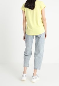 T-shirt giallo a maniche corte, taglio morbido, abbinato a jeans dritti di un blu chiaro e sneakers argento con suole bianche. Tessuto a trama liscia.