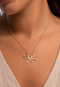 Goldener Sonnenstrahl-Halskette mit gewellten Strahlen und einem zentralen Halbmond-Detail, verziert mit klaren Kristallen an einer dünnen Kette.