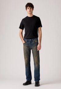 Black short-sleeve t-shirt paired with faded blue jeans; jeans show light distressing, two front pockets, and a button fly. Black boots.