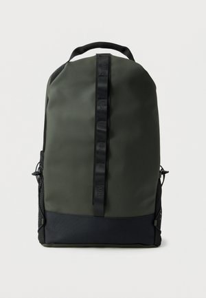 Tume roheline ja must seljakott, millel on vertikaalne must rihm ja võrgust küljetaskud, kujutatud ühevärvilise heleda tausta ees.