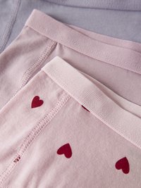 Kaks pruuni puuvillast kokkupandud aluspesu paari, üks lihtne ja teine trükitud väikeste punaste südametega pehmel kangal.