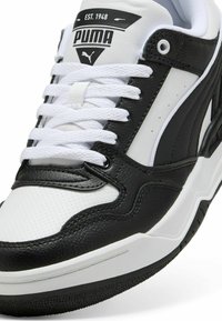 Tenis Puma alb-negru cu partea superioară din piele texturată, șireturi albe, manșetă căptușită și talpă din cauciuc cu un model cu crampoane. Logo pe limbă.